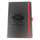 A black notebook with a red elastic band, featuring a logo of lips with dripping gloss and the text GlossTone High-Impact Branding on the cover.