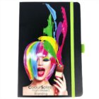 A notebook with a black cover featuring an image of a woman with rainbow-colored hair and a paintbrush, splattering matching paint colors. The text reads, ColourSplash High-Impact Branding. A lime green elastic band holds the notebook.