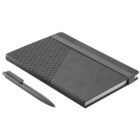 A closed black notebook with a textured triangular pattern on the cover lies on a flat surface. A black pen with a similar texture rests beside it. An elastic band is wrapped around the notebook to keep it closed.
