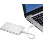 A silver external hard drive is connected to a laptop via a white USB cable. The laptop screen displays a blue background with small white icons.