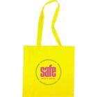 A bright yellow tote bag with long handles features a bold gray circle logo. Inside the circle, the word safe is written in large pink letters, with the phrase see. act. fix. everyday. underneath in smaller gray text.