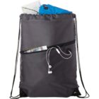 A gray drawstring backpack with a front zipper pocket containing a map, blue fabric, a small magazine, and white earphones. The main compartment appears open, showing some contents partially visible.