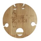 A round, wooden board with a surfboard motif and the words Surf Beach engraved on it. It features four circular indentations and a slot, possibly for holding wine glasses and a bottle.
