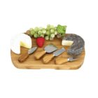 A wooden cheese board with two cheese rounds, one white and one black-coated, both partially cut. Four cheese knives with wooden handles are on the board. Green grapes and a strawberry embellish the display.