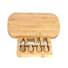 A bamboo cheese board with a slide-out drawer containing four cheese knives with wooden handles neatly stored in custom slots. The board has a smooth, light wood finish, and the setup is designed for serving cheese.
