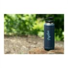 A dark blue thermos bottle with the word Papillon in white lettering is resting on a rock. The background shows blurred greenery, suggesting an outdoor setting.