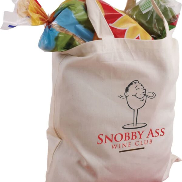 A beige tote bag with Snobby Ass Wine Club printed on it. The bag is filled with groceries, including a loaf of sliced bread in colorful packaging and leafy greens.