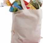 A canvas tote bag filled with colorful packaged food items, including a loaf of sliced bread and a green fruit or vegetable, possibly cabbage or lettuce, visible at the top.