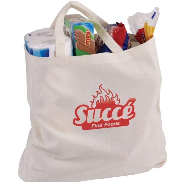 A white canvas shopping bag with Succé Fine Foods logo is filled with various grocery items, including toilet paper and food packages, with some items sticking out of the top.