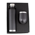 A matte black insulated bottle and a matching tumbler are neatly placed in a foam-lined box. Both items have stainless steel accents and are arranged vertically, with the bottle on the left and the tumbler on the right.