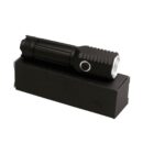 A compact black flashlight with a textured grip and a side button is placed on top of a matching black rectangular box. The flashlight is positioned diagonally across the box.