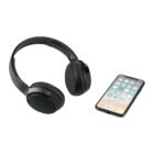 Black over-ear wireless headphones are placed next to a smartphone displaying app icons on its screen, set against a plain white background.