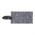 A rectangular gray felt luggage tag with a black leather strap and a metal buckle. The tag features a small round metal button on the front.