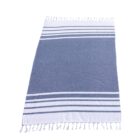 Rectangular, blue and white fringed towel. The towel features two sections of horizontal white stripes near the edges, with a solid blue center. The fringes are short and white, located along the shorter sides of the towel.