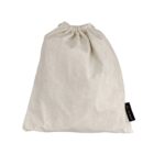 Beige drawstring cloth bag, lightly wrinkled, resting on a white background. A small black tag with white lettering is attached to the side of the bag.