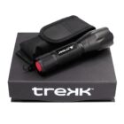 A black flashlight with red detailing on the button, branded Trek, is placed on a black box. The flashlight is accompanied by a black, textured carrying case.