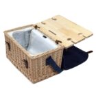 Open wicker picnic basket with a folding wooden lid. The basket has an insulated compartment lined with fabric, metal hinges, and leather straps. A navy blue cloth covers the front pocket area.
