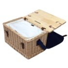 A woven picnic basket with a wooden lid slightly open, revealing a white fabric lining inside. The basket features leather straps and a navy blue shoulder strap. The wooden lid has carved sections for securing items.
