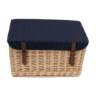 A wicker picnic basket with a navy blue fabric lid secured by two brown leather straps.