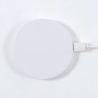 Round white wireless charger with a USB cable attached, on a white surface.