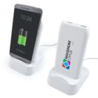 Smartphone on wireless charging stand next to branded power bank on a stand.