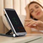 Person touching a phone on a stand, with a charging icon displayed.