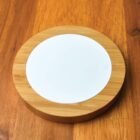 Round wooden coaster with a white ceramic center on a wooden table.