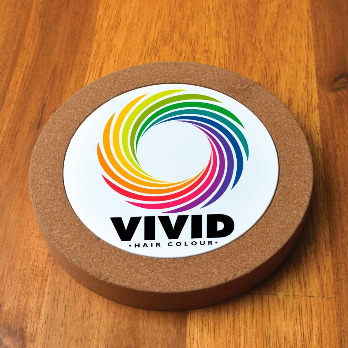 Circular coaster with colorful swirl design and text Vivid Hair Colour on wooden surface.