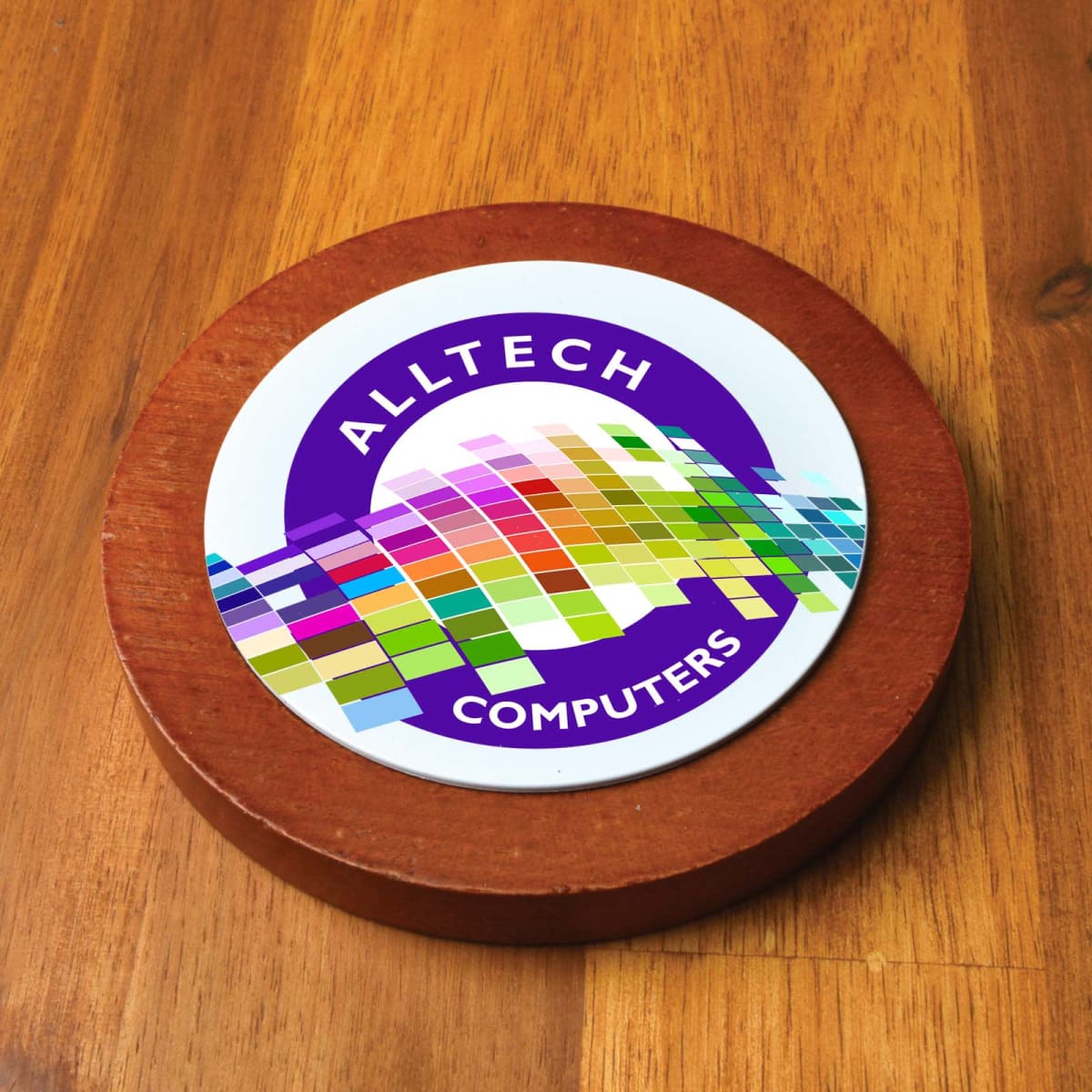Round sticker on wooden surface with colorful buildings and ALLTECH COMPUTERS text.