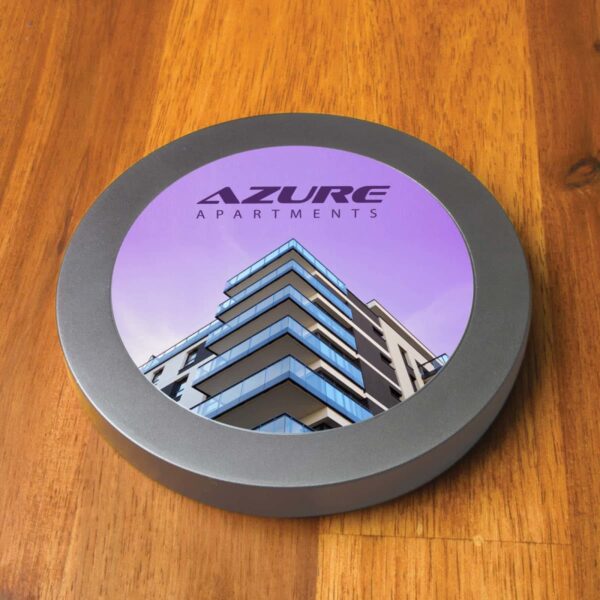 Round coaster with Azure Apartments image and logo on a wooden table.