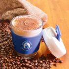 Coffee with cinnamon in a reusable cup, surrounded by coffee beans and a burlap sack.