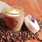 Latte in a glass cup surrounded by coffee beans on a wooden surface.