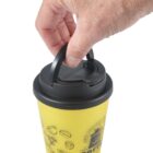 Hand lifting black lid on a yellow coffee cup with illustrations.