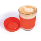 Glass of latte with latte art, orange lid, and matching sleeve.