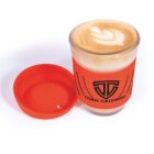 Glass of coffee with latte art, orange lid, and Titan Caldwell logo on sleeve.