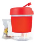 Red and clear snack container with colorful candy beside it.