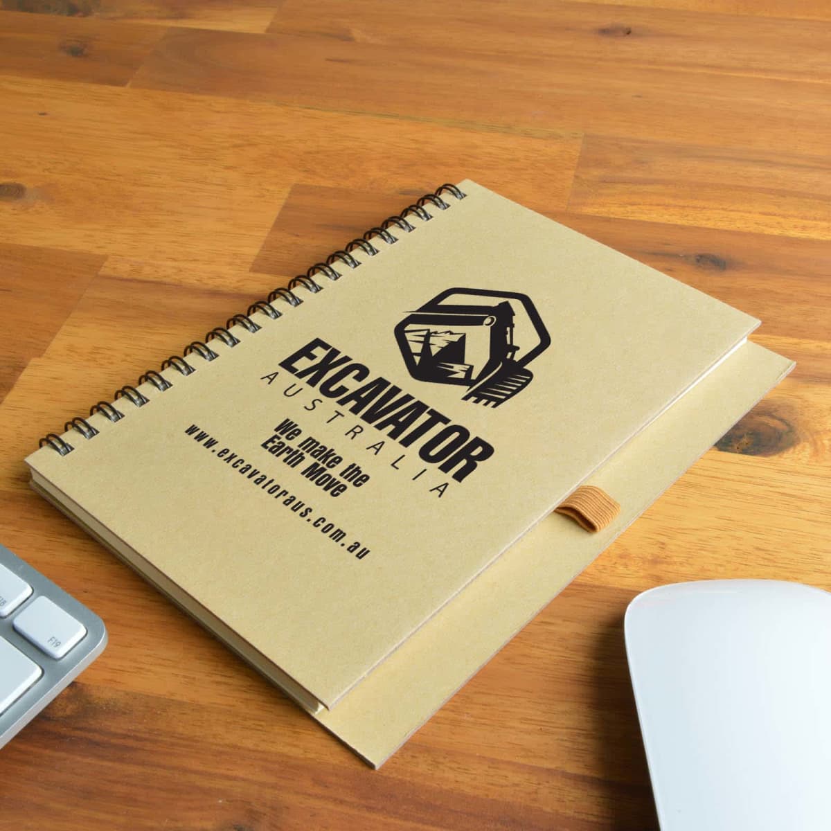 Spiral notebook with Excavator Australia logo on wooden desk beside a keyboard and mouse.