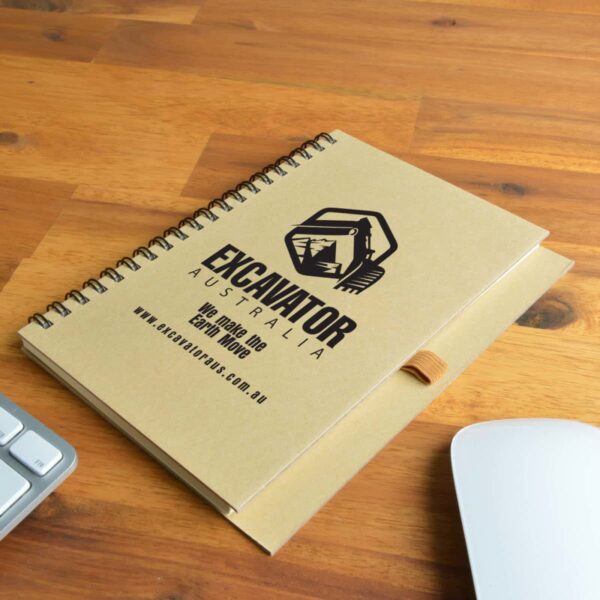 Spiral notebook with Excavator Australia logo on a wooden desk beside keyboard and mouse.