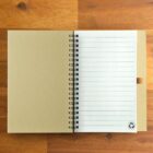 Open spiral notebook with lined pages and recycling symbol on a wooden surface.