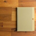 A closed spiral notebook on a wooden table.
