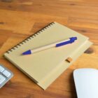 Notebook and pen on a wooden desk beside a keyboard and mouse.