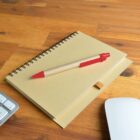 Notebook and red pen on a wooden desk with a keyboard and a white mouse.