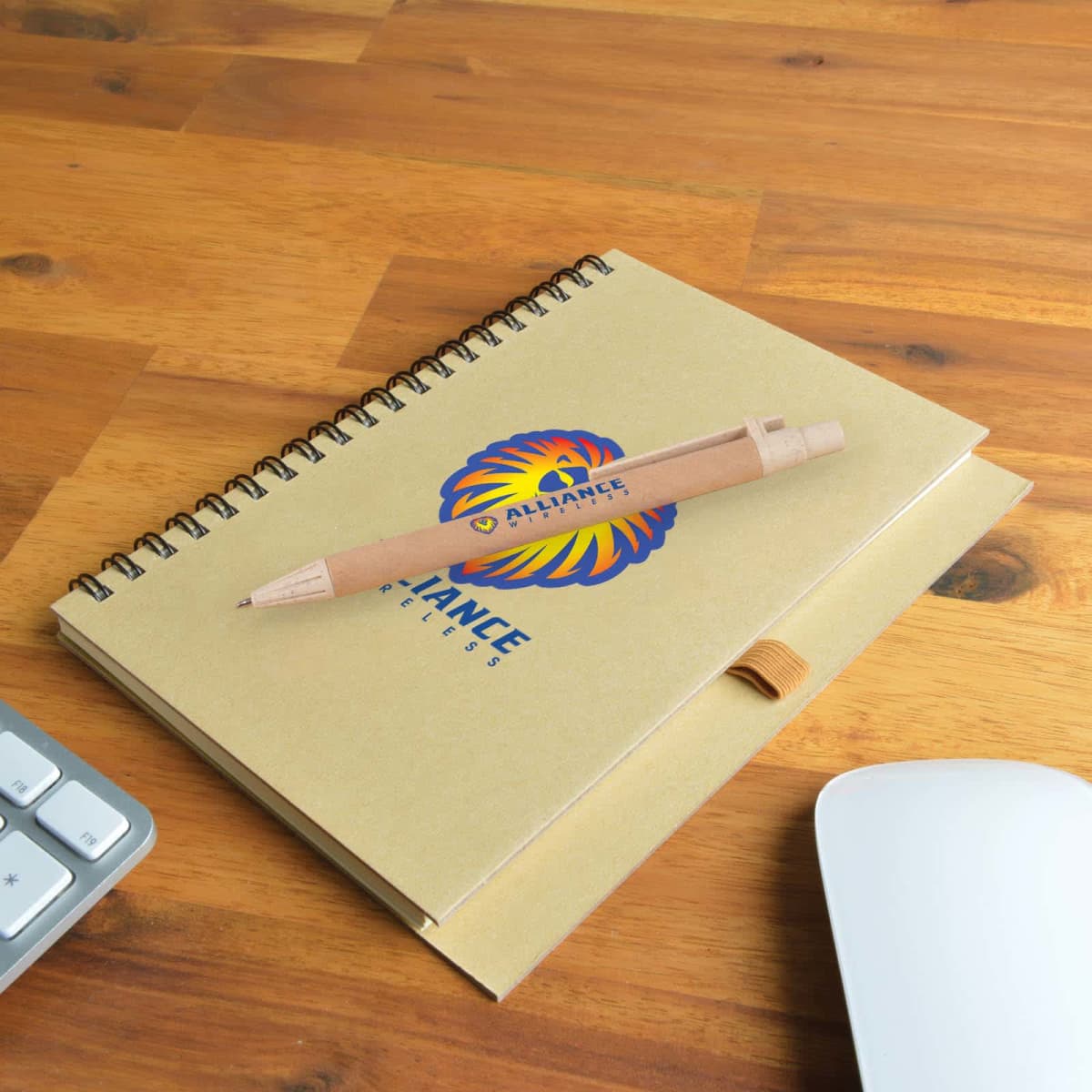 Notebook with a logo and a pen on a wooden desk, next to a keyboard and mouse.