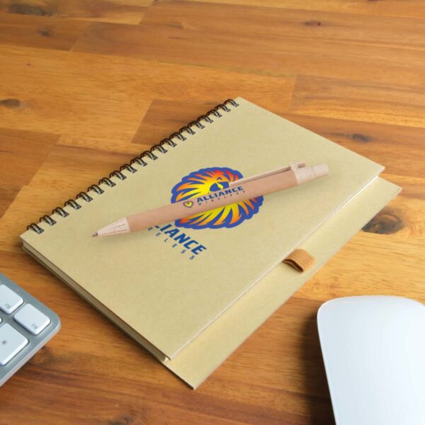 Spiral notebook with pen on a wooden desk, near a keyboard and mouse.