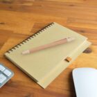 Notebook and pen on a wooden desk with part of a keyboard and mouse visible.