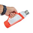 Hand holding a clear water bottle with a red strap and silver cap.