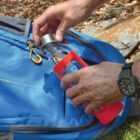Person placing a water bottle into a blue backpack outdoors.