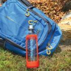 Blue backpack and DeltaWater bottle on grass, near a bed of stones.