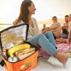 Group enjoying a picnic on the beach with an open lunch bag in the foreground.