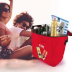 A picnic scene with friends, a red cooler bag filled with drinks, a cereal box, on a sunny day.
